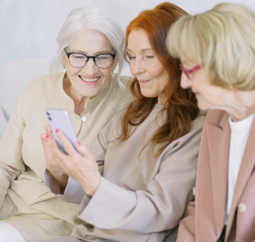 Feminine presenting people sat three aside videochatting with someone on a phone.